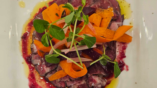 A photo of a raw sirloin steak with a jar of flaky salt and a jar of peppercorns to the side.