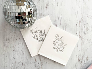 Silver baby it's cold outside cocktail napkins with festive design, featuring winter-themed text and elegant pattern by EnFete LLC.