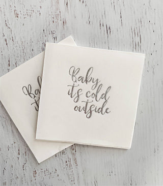 Set of silver cocktail napkins with "Baby, It's Cold Outside" printed in stylish font, perfect for winter parties and gatherings.