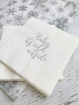Set of silver "Baby, It's Cold Outside" cocktail napkins by EnFete, LLC, featuring festive winter design for parties.